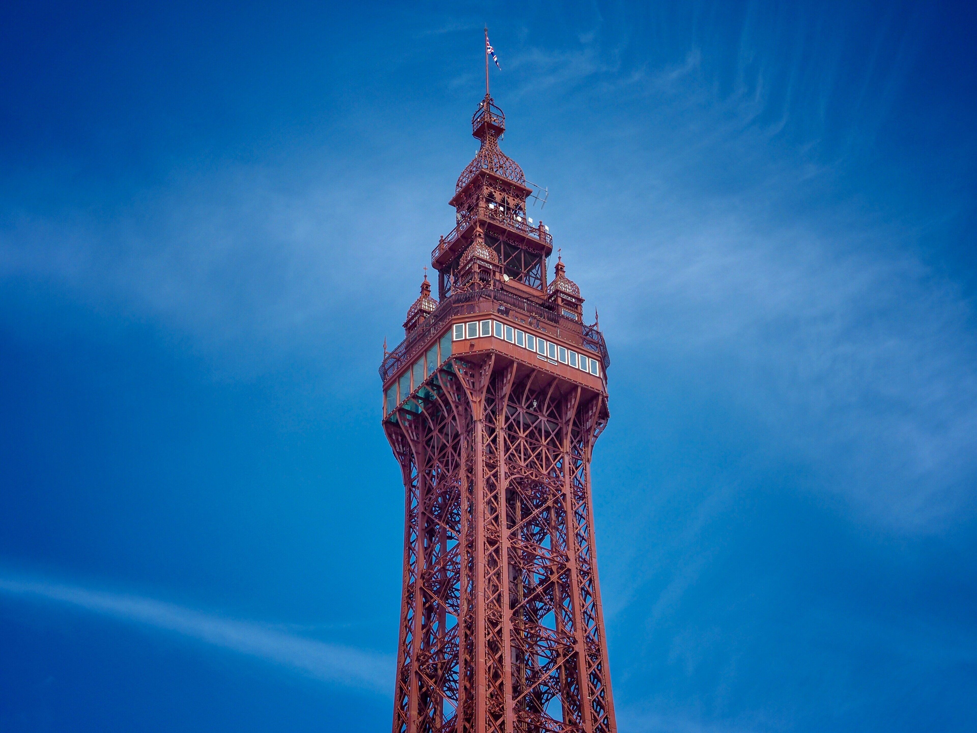 A tall, intricately designed tower with a spire and flag, set against a clear blue sky.