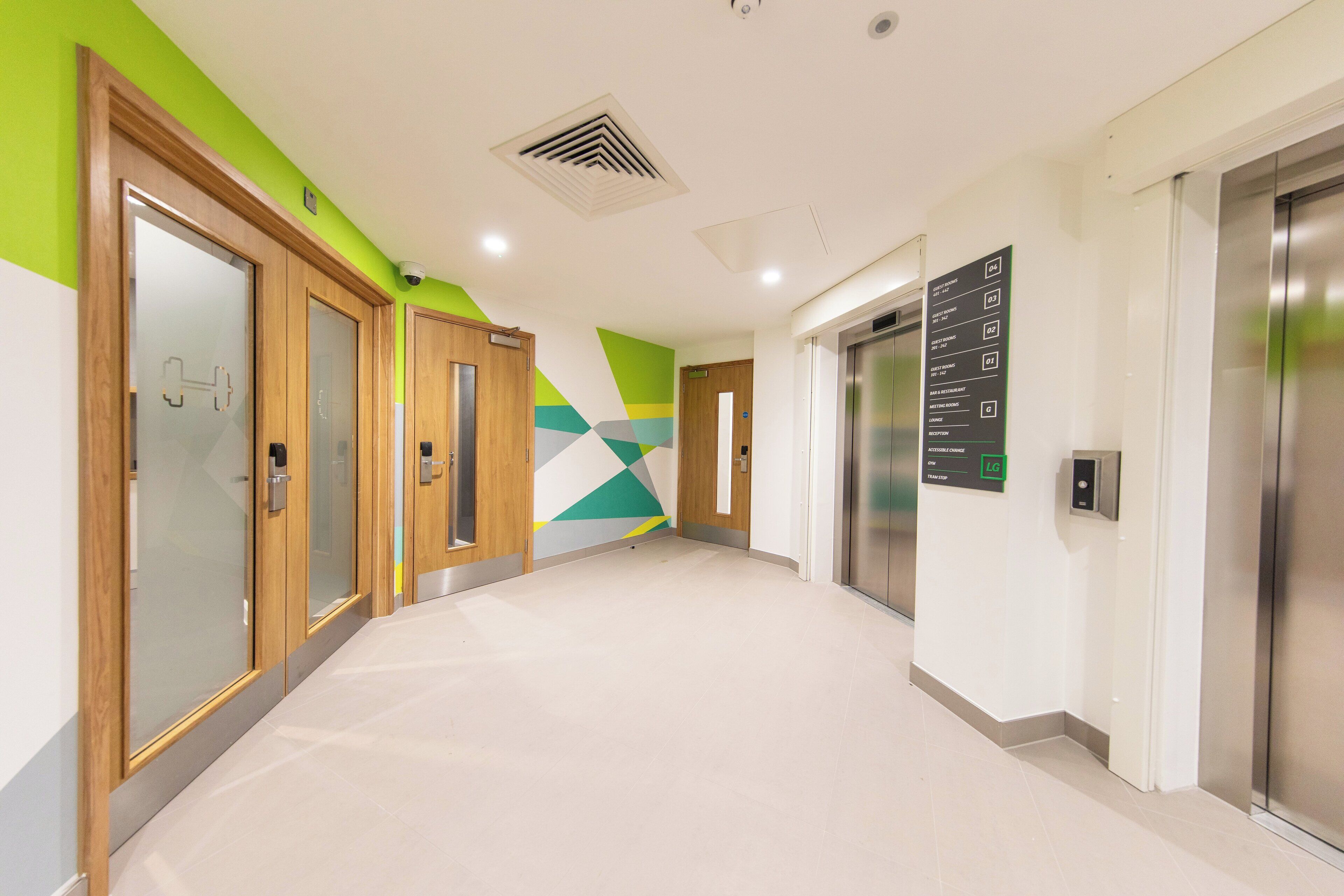 A modern hallway with a geometric wall design, wooden doors, and an elevator.