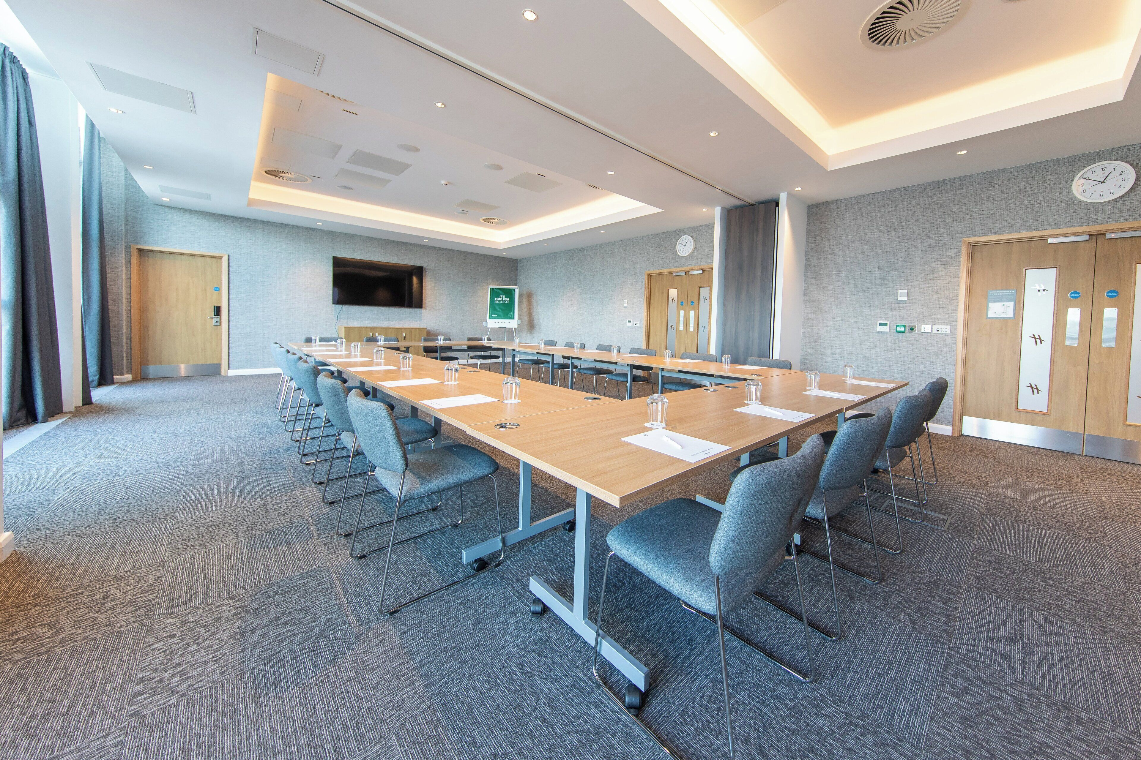 A conference room with a long table, chairs, a clock, and a TV on the wall.