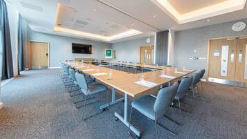 A conference room with a long table, chairs, a clock, and a TV on the wall.