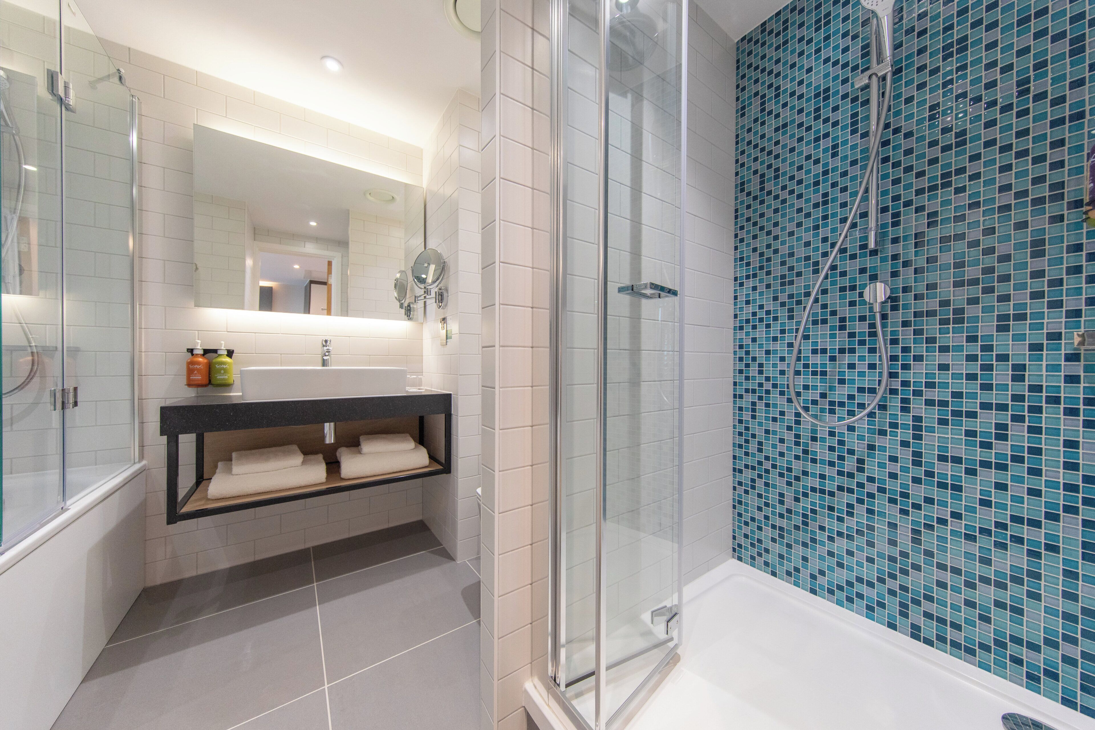 A modern bathroom with a glass shower enclosure, a white sink with a mirror, and a tiled wall with a blue mosaic pattern.