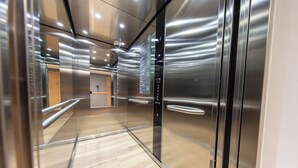 A modern elevator interior with metallic walls, a wooden floor, and a digital display panel.