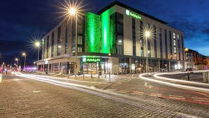 A Holiday Inn hotel with a modern facade, large windows, and a prominent green accent on the side.