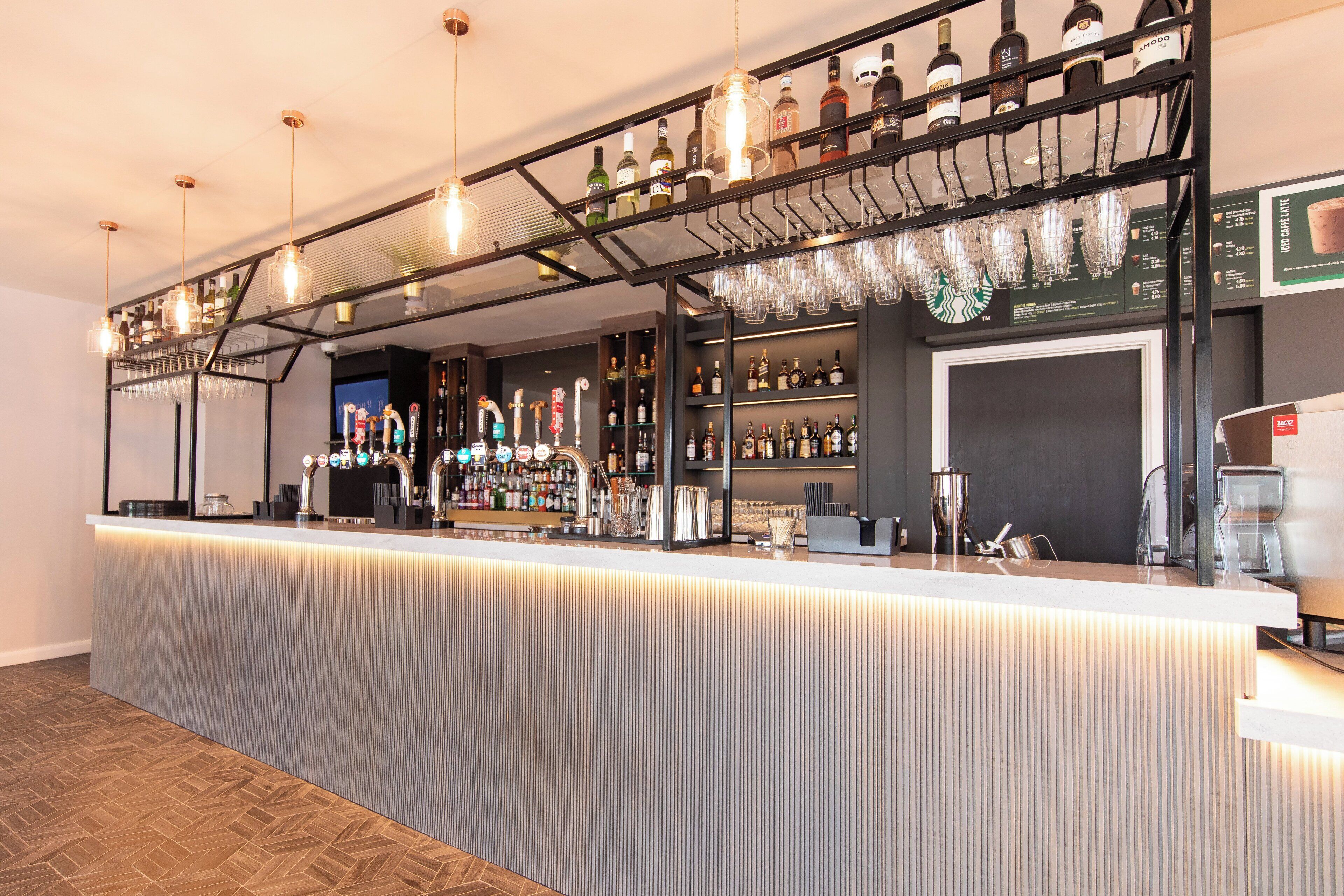 Un espace bar doté d’un long comptoir, d’étagères remplies de bouteilles et de verres suspendus.
