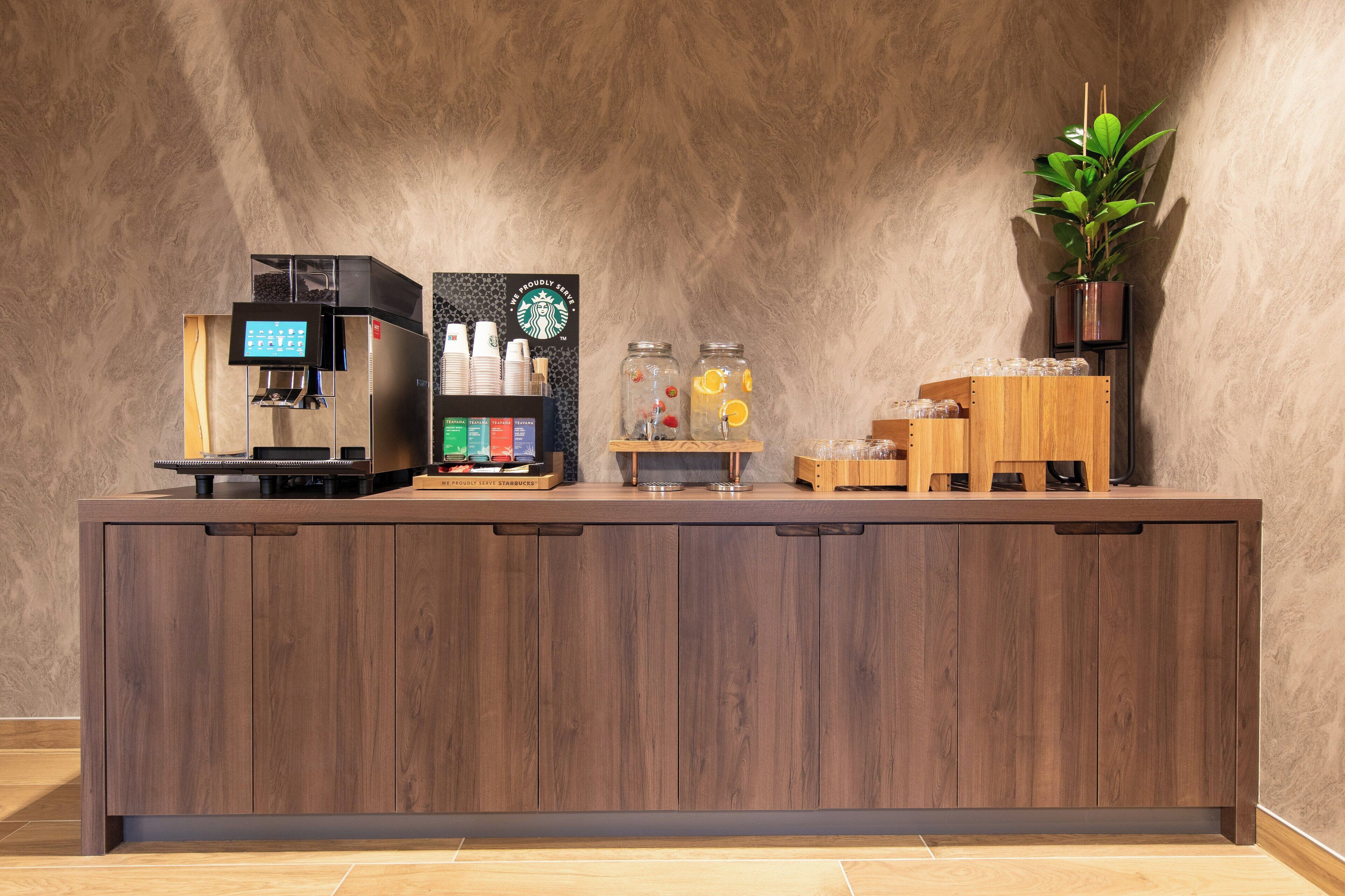 A wooden reception desk with a coffee machine, a Starbucks sign, and a plant.