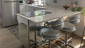 A modern kitchen with a stainless steel refrigerator, a built-in oven, a microwave, and a sink. There are four bar stools with metal frames and cushioned seats. The kitchen has white cabinets and a large window providing natural light. - Dog-Friendly Home - 1.5 Miles from Red Rocks Amphitheater (Morrison)