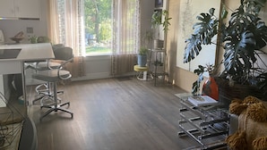 A modern living room with a wooden floor, a dining area with a table and chairs, a large window with curtains, and several potted plants. - Dog-Friendly Home - 1.5 Miles from Red Rocks Amphitheater (Morrison)