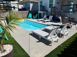 Um quintal com piscina, cadeiras de descanso e uma pequena área de deck.