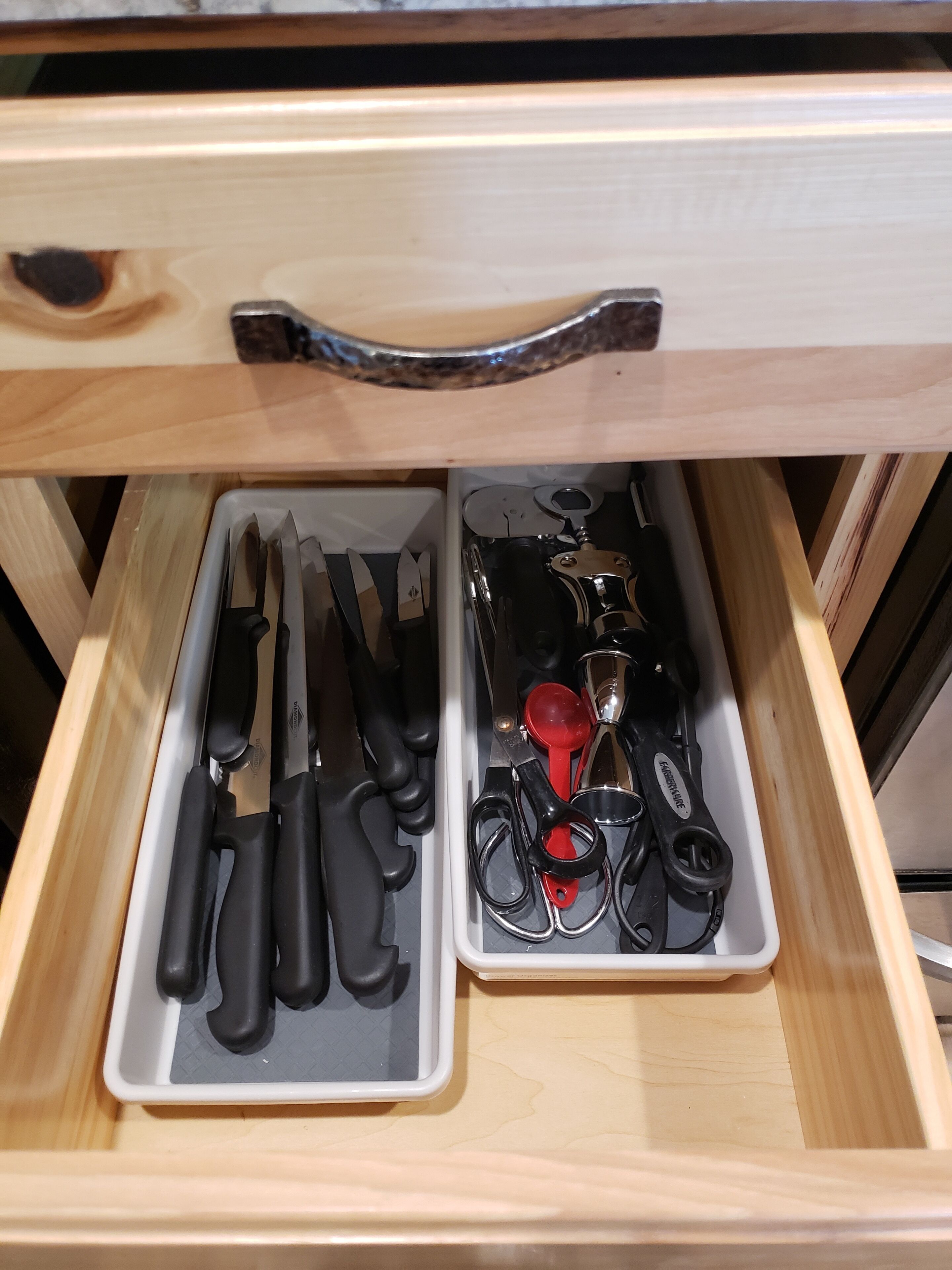 A drawer with two compartments: one with black-handled knives and the other with scissors and measuring tools.