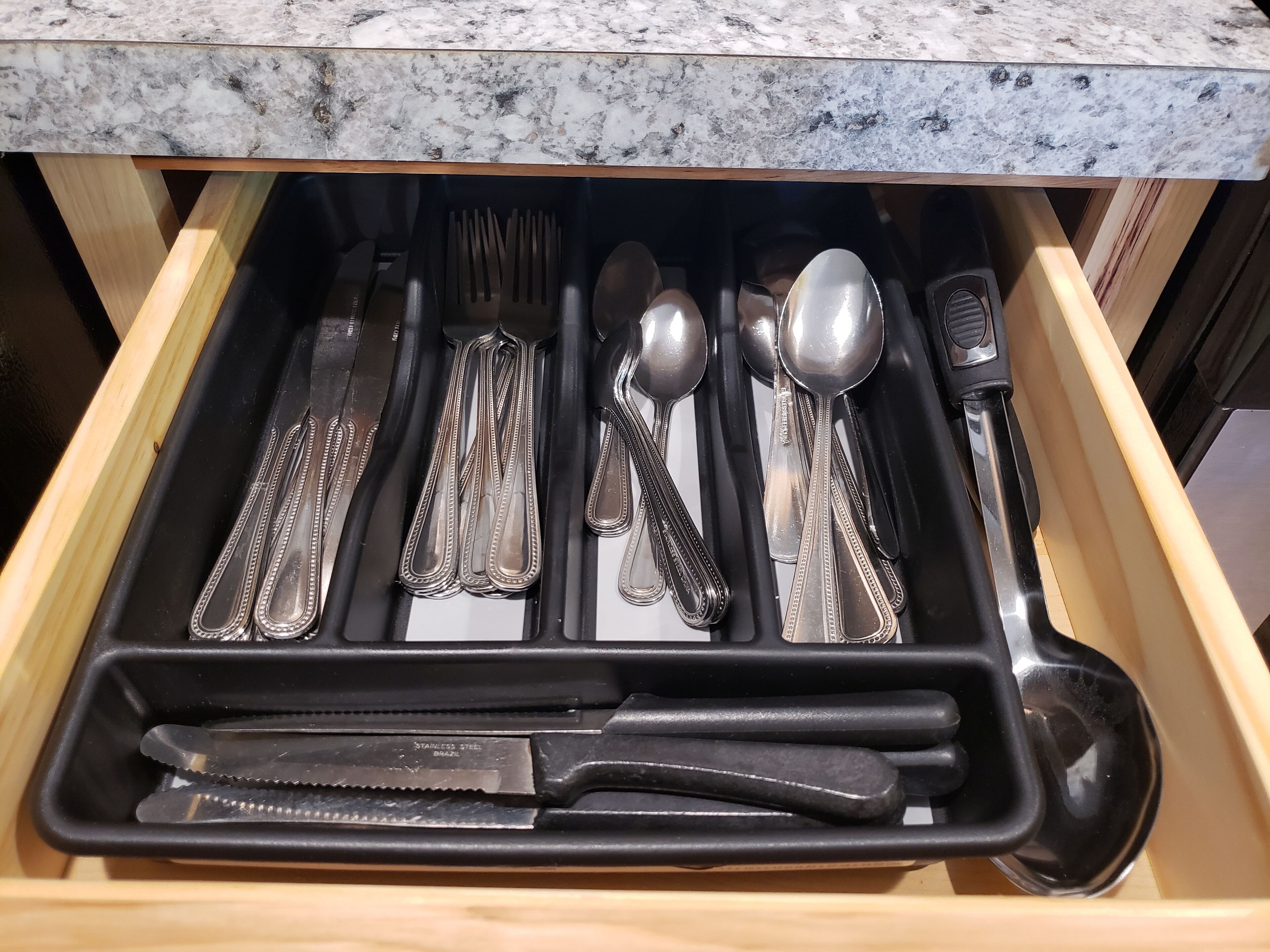 A drawer with neatly organized stainless steel cutlery and utensils.