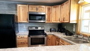 Una cocina con armarios de madera, un refrigerador negro, un microondas, una estufa, un tostador y un fregadero.