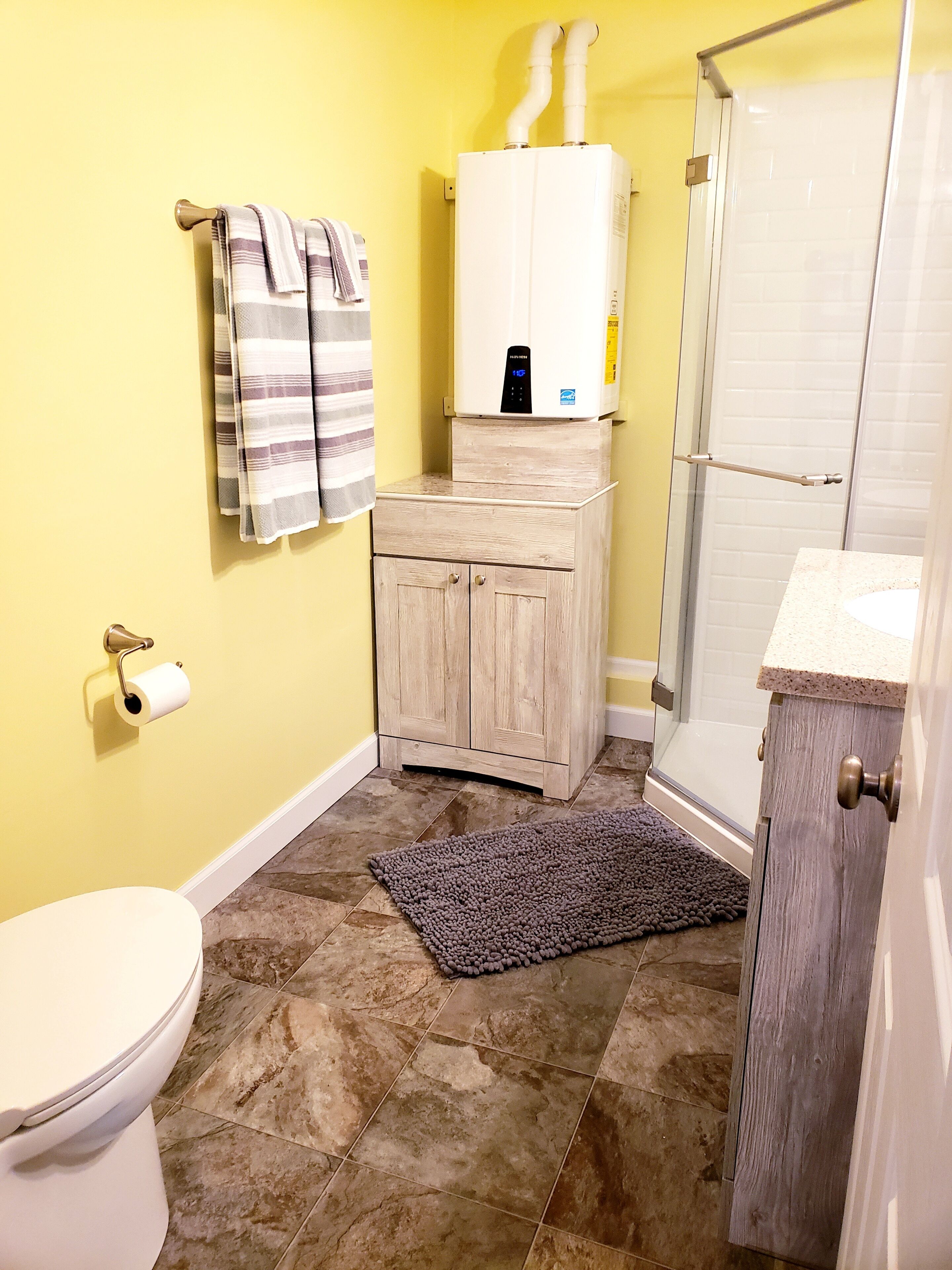 Une salle de bain comprenant des toilettes, une douche, un porte-serviettes avec des serviettes, un meuble et un tapis.