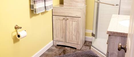 Une salle de bain comprenant des toilettes, une douche, un porte-serviettes avec des serviettes, un meuble et un tapis.