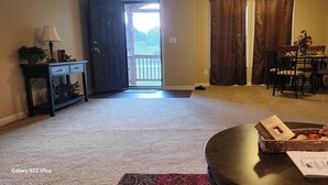 A living room with a dark wooden coffee table, a wicker basket, and a welcome card. There is a dining table with chairs and a lamp on a side table. - Mountain Home,  PET FRIENDLY!!  Anderson Farms@Fall Creek Falls State Park  (Pikeville)