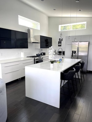 A modern kitchen with a central island, dark flooring, and a large window.