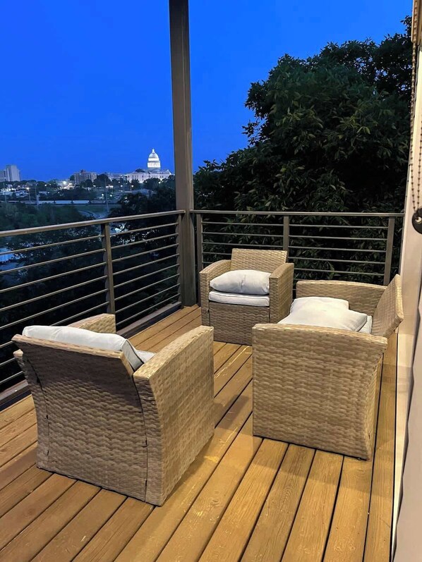 A balcony with wicker furniture and a view of a cityscape at dusk.