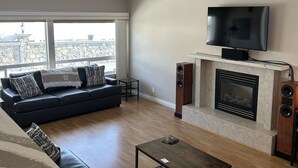Un salon moderne avec un canapé noir, une table basse, une cheminée et un téléviseur fixé au mur.