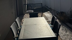Une terrasse extérieure avec une table et des chaises, une clôture blanche et une vue sur des montagnes lointaines sous un ciel dégagé.
