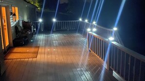 A wooden deck with a railing, a small seating area with chairs, and a door leading to a building. - The Bunkhouse Retreat /Sleeps 15/7BR/5BA/4 Private Acres (Kings Mountain)