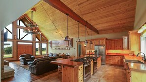 A spacious kitchen with wooden cabinets, a large island with a stove, and a dining area with a leather couch. - The Bunkhouse Retreat /Sleeps 15/7BR/5BA/4 Private Acres (Kings Mountain)