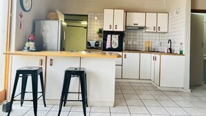 A kitchen with white cabinets, a wooden countertop, two black stools, and a clock on the wall. - Lovely 1 bedroom Loft in the Heart of Walvisbay. (Walvis Bay)