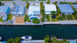 An aerial view of a waterfront property with multiple buildings, a swimming pool, and a dock with boats.