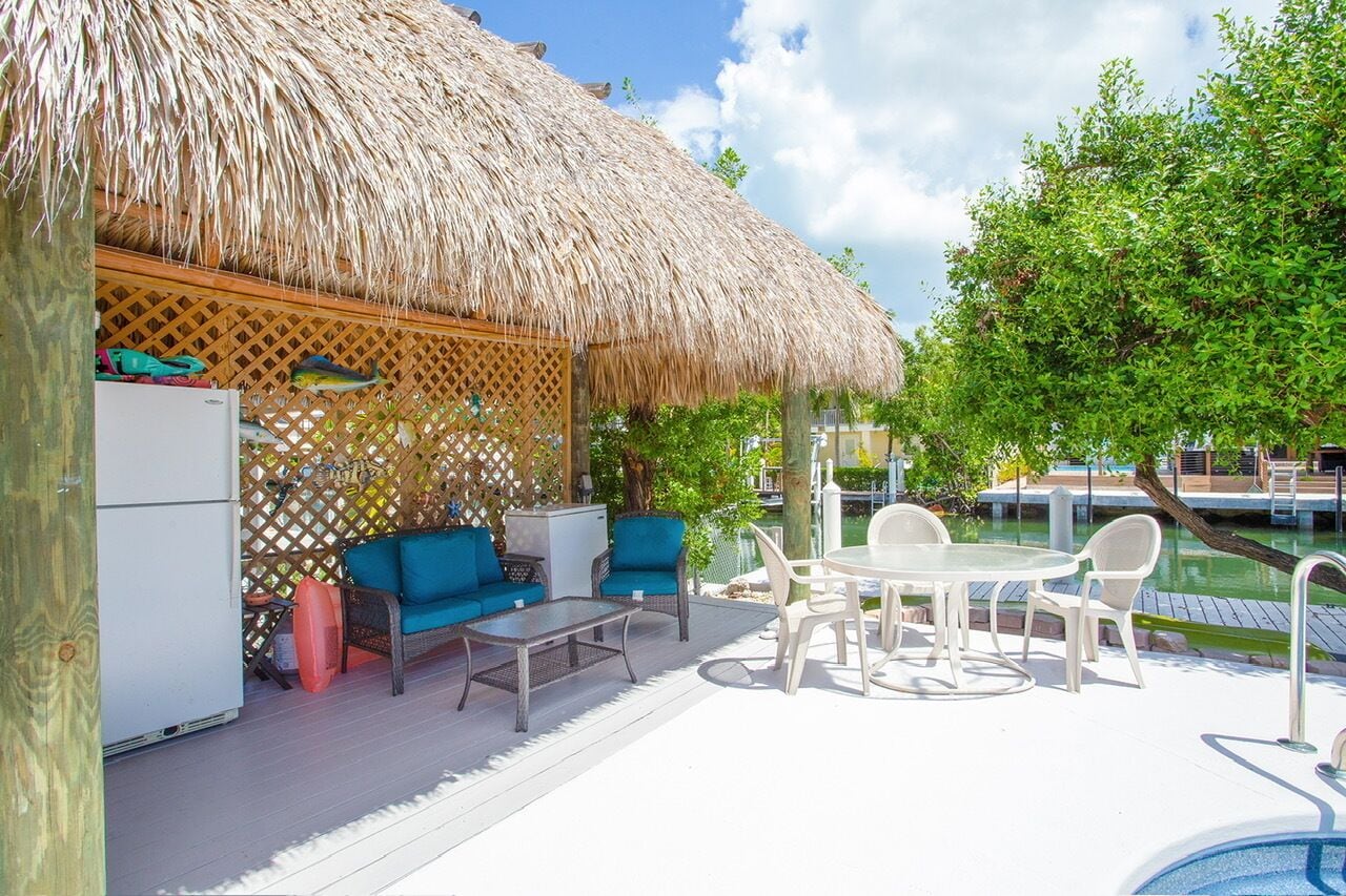 Un espace aménagé au bord de la piscine, doté d’une structure à toit de chaume, de sièges d’extérieur et d’une piscine.