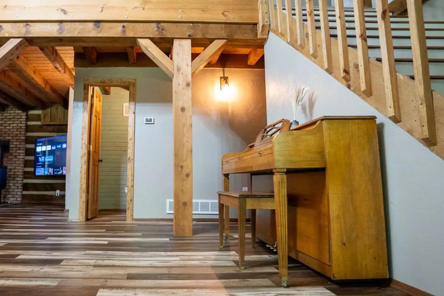 Una habitación amplia con una escalera de madera, un piano y un televisor en la pared.