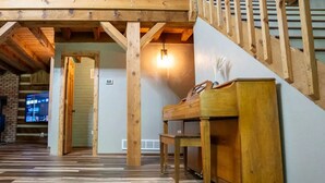 Ein geräumiges Zimmer mit einer Holztreppe, einem Klavier und einem Fernseher an der Wand.
