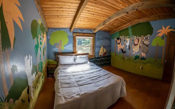 Un dormitori amb sostre de fusta, un llit i parets decorades amb murals de temàtica de la selva.