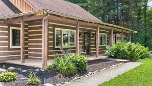Eine Blockhütte mit überdachter Veranda, großen Fenstern und einem angelegten Garten.