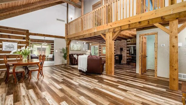 Ein geräumiges Zimmer mit Holzboden, einem Esstisch mit Stühlen, einem Ledersofa und einem Balkon mit Holzbalken.