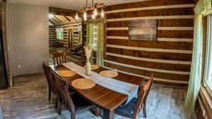 Ein Essbereich mit Holztisch und -stühlen, einer Vase mit Trockenpflanzen und einer Holzwand mit dekorativem Zierpaneel.