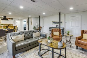 A modern living room with a leather sofa, a coffee table, and a dining area in the background. - Alabama Retreat w/ Private Pond, Deck & Pool Table (Eutaw)