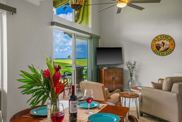 A dining area with a table set for two, a bottle of wine, and a glass of red wine. There is a view of a green landscape through a glass door.