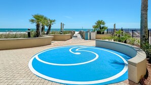 Ein gepflasterter Weg führt zu einem Strand mit Palmen und einem blauen, kreisförmigen Design auf dem Boden.