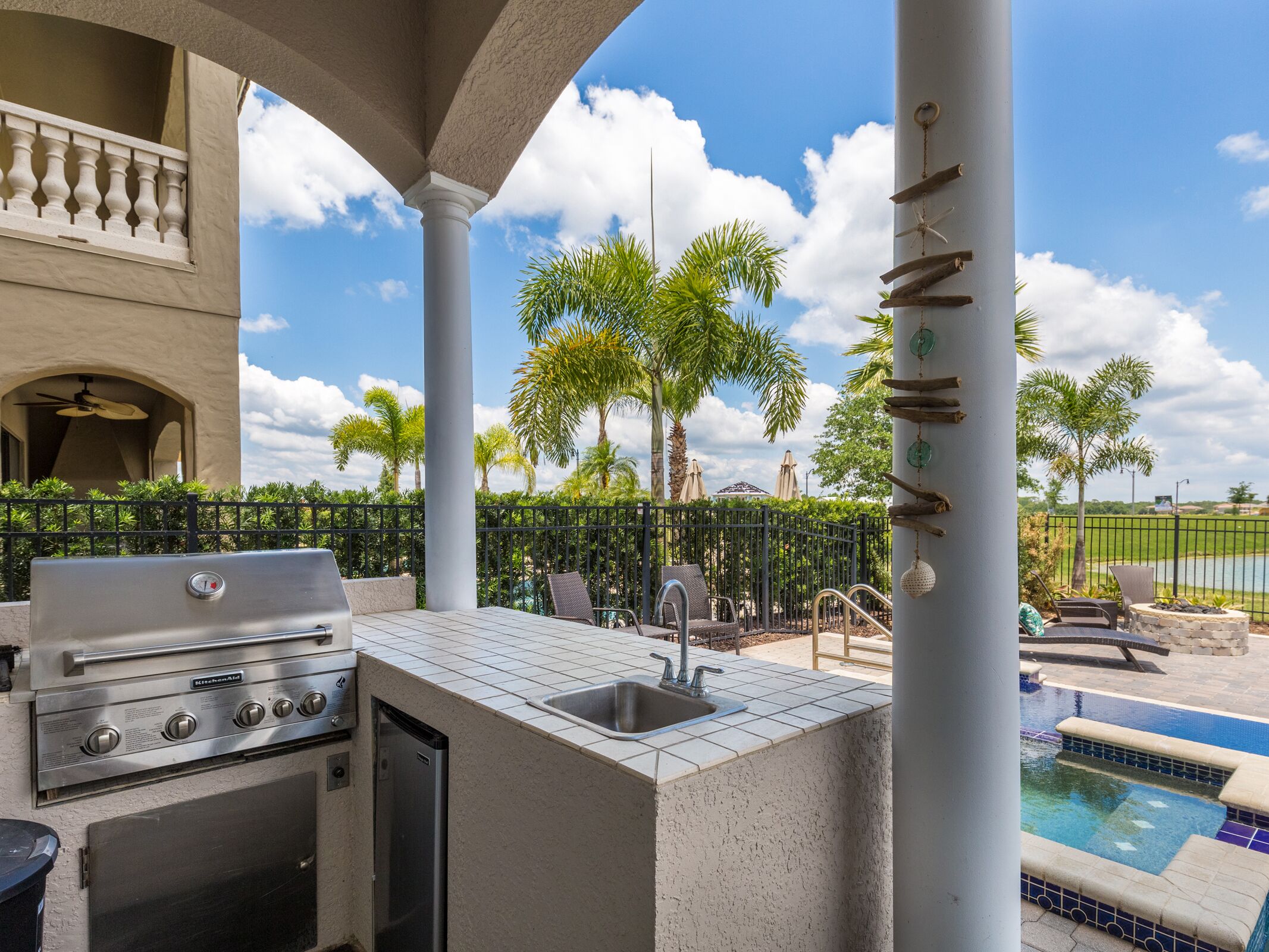 An outdoor kitchen area with a grill, sink, and a poolside lounge.