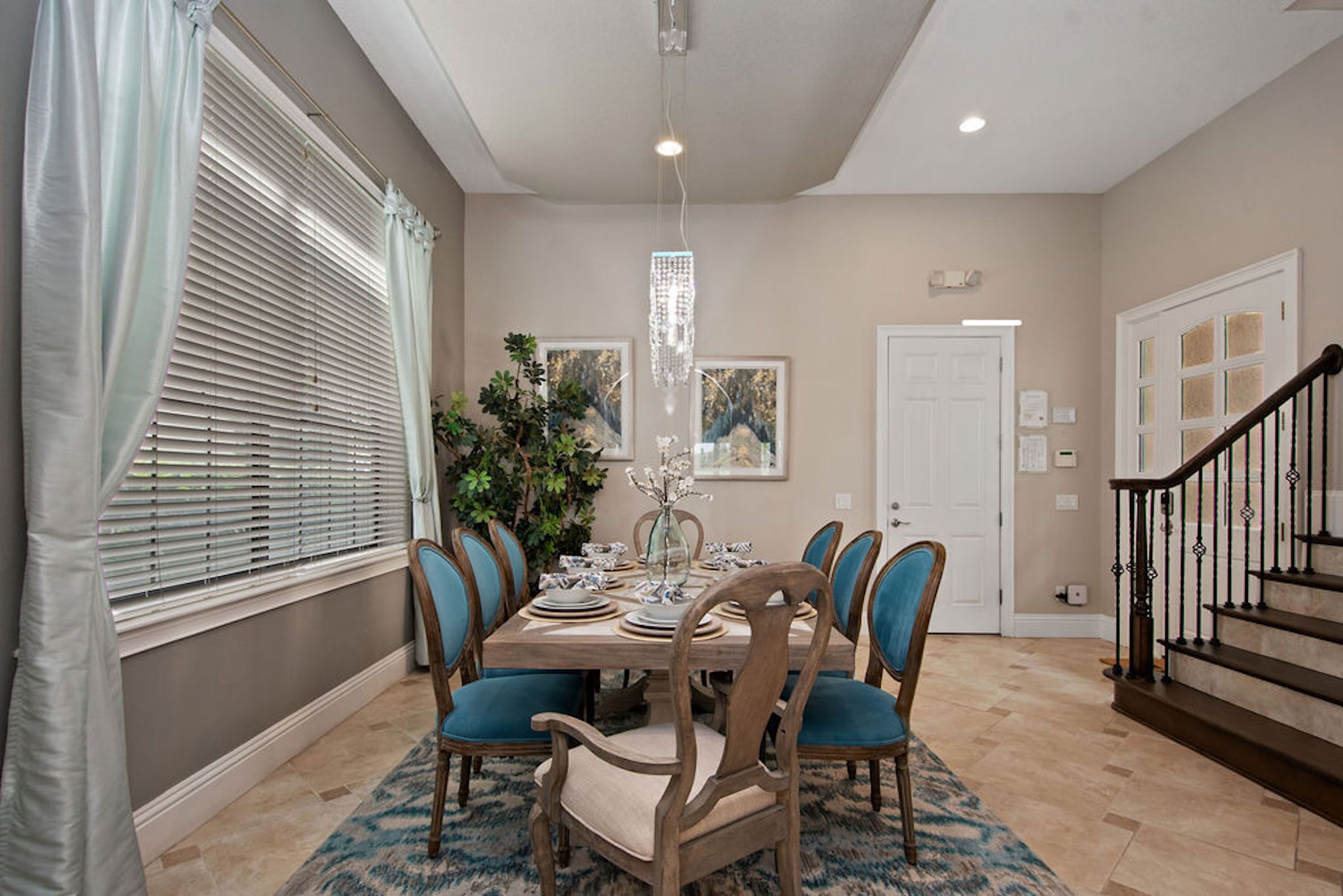 A dining room with a wooden table set for six, surrounded by six chairs with blue cushions.