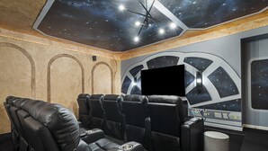 Une salle de cinéma privée avec des fauteuils en cuir inclinables, un grand écran et un plafond décoré d’un motif étoilé.