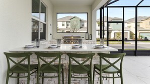 Une terrasse extérieure équipée d’un barbecue, de trois chaises et d’une table dressée pour les repas.