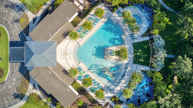 Vue aérienne d’un hôtel doté d’une piscine centrale, entourée de palmiers et de chaises longues.