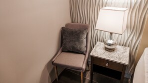 Un coin d’une chambre d’hôtel avec un fauteuil rembourré, une table de chevet au plateau en marbre et un mur orné d’un motif ondulé.