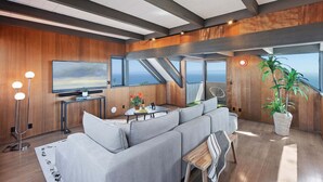 Un interior modern amb un sofà, una televisió i una finestra gran amb vista al mar.