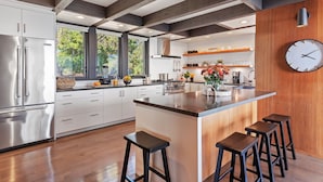 Une cuisine moderne dotée d’un îlot central, d’appareils électroménagers en acier inoxydable et d’éléments décoratifs en bois.