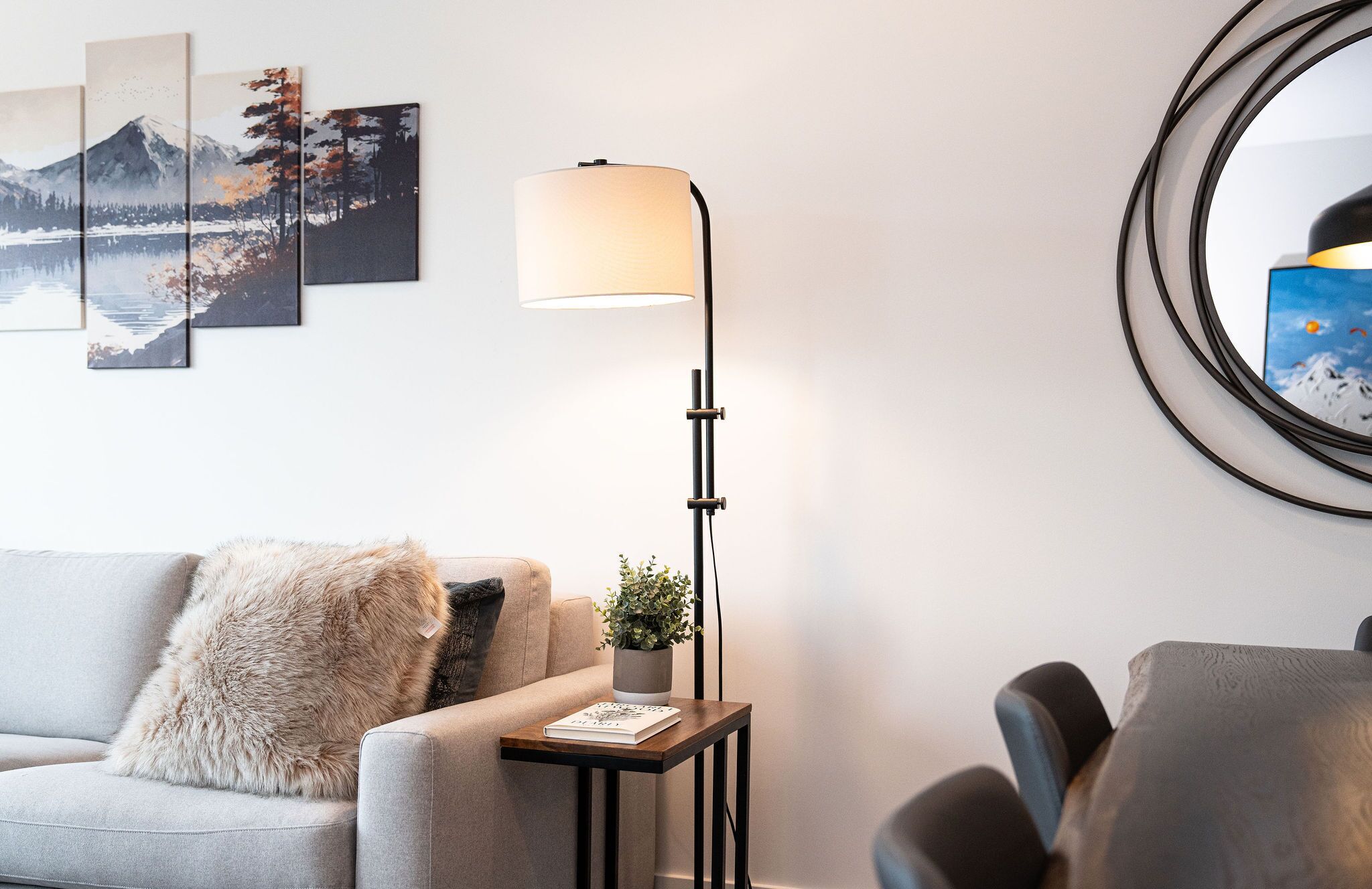 A modern living room with a sofa, a floor lamp, a small table with a plant, and artwork on the wall.