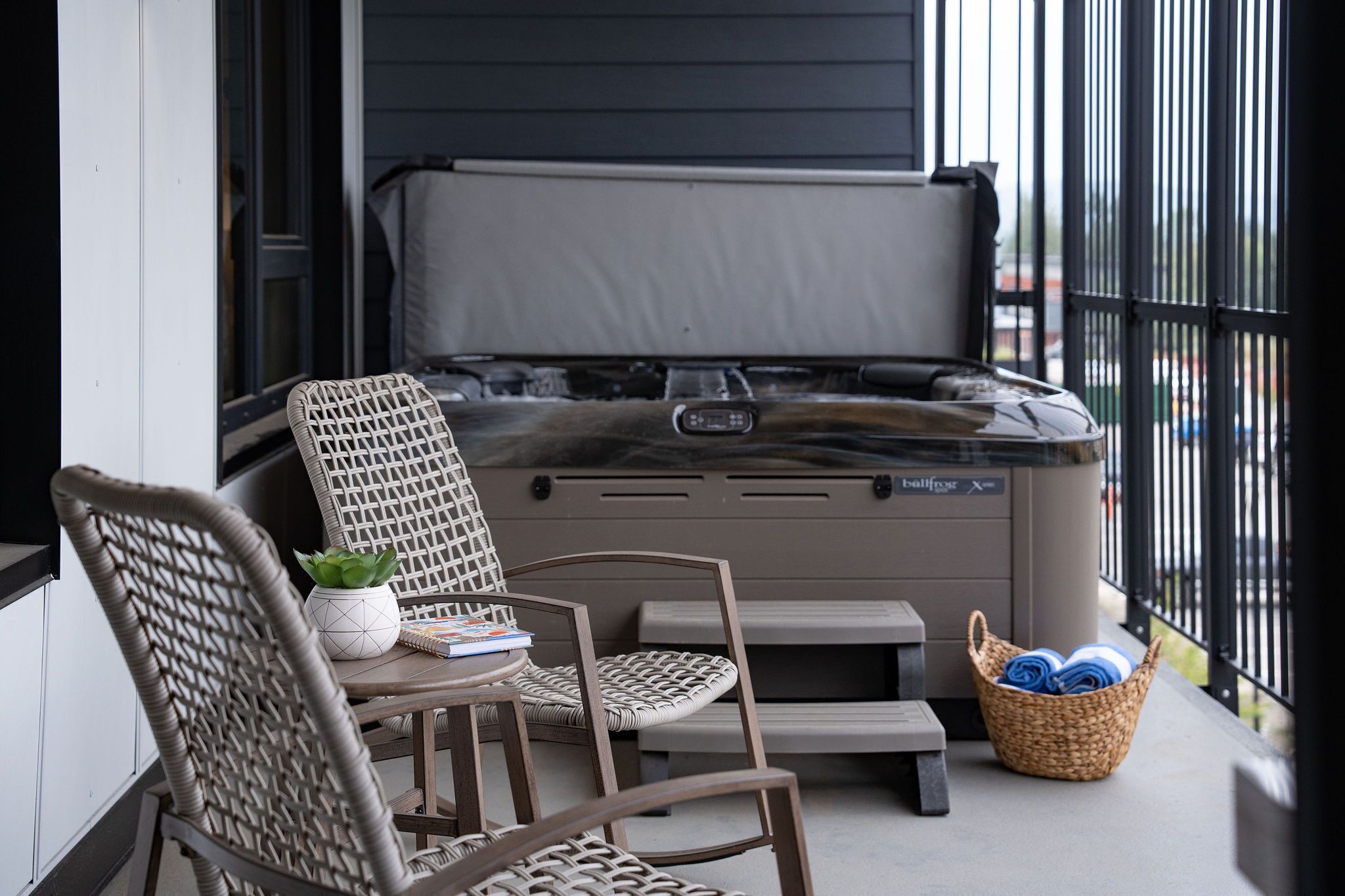 Ein Whirlpool auf einem Balkon mit Korbstühlen und einem Wäschekorb voller Handtücher.