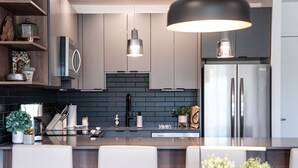 A modern kitchen with a black backsplash, stainless steel appliances, and a central island with seating. - Revylation by Revelstoke Vacations (Revelstoke)