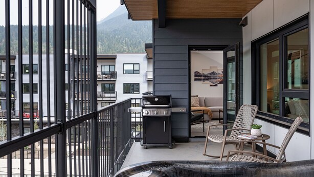A balcony with a grill, wicker chairs, and a view of a mountain. - Revylation by Revelstoke Vacations (Revelstoke)