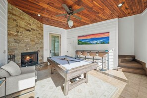 A pool table in a room with a stone fireplace, a ceiling fan, and a painting on the wall.