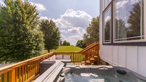 Un bain à remous sur une terrasse dotée d’une rambarde en bois, d’un escalier et offrant une vue sur un paysage verdoyant.
